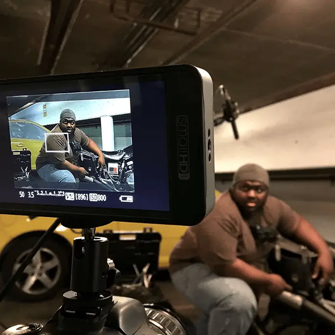 Video monitor mounted on camera showing a guy working on motorcycle