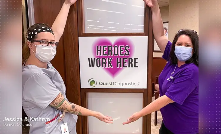 Two nurses standing either side of a Heroes Work Here sign